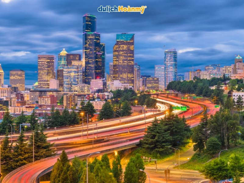 Toàn cảnh thành phố Seattle lung linh về đêm với Space Needle nổi bật, thể hiện sự phát triển đô thị và hấp dẫn du lịch, một yếu tố quan trọng trong giao lưu kinh tế.