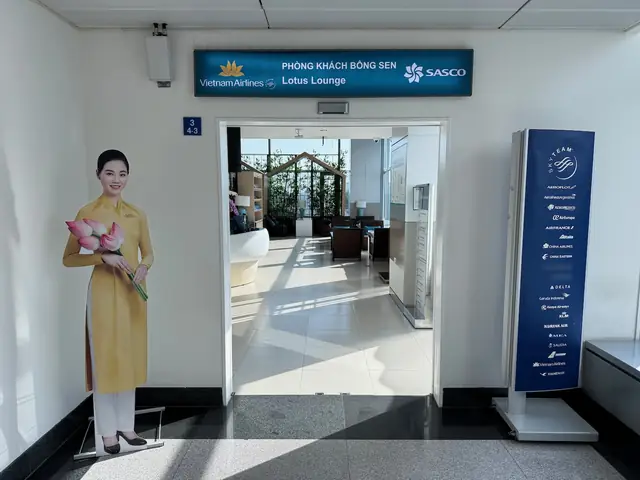 Vietnam Airlines Lotus Lounge Entrance With A Staff Cutout Holding Lotus Flowers, Featuring Lounge Seating And Greenery In The Background, Showcasing The Airline's Hospitality And Amenities.